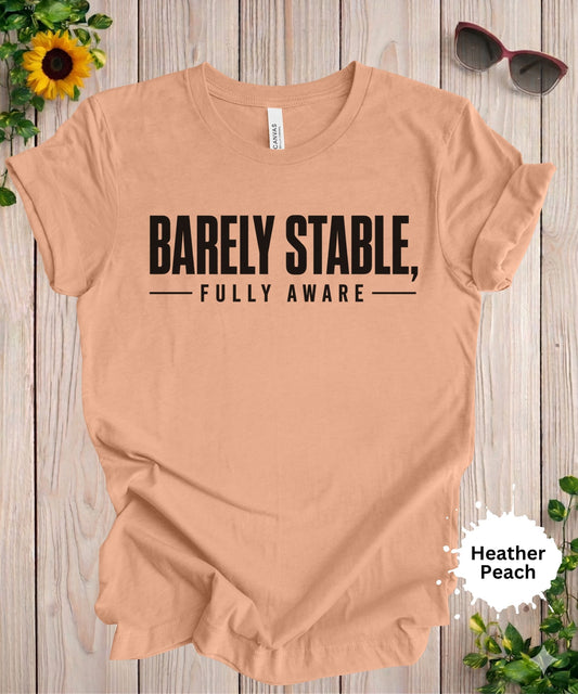 Women’s graphic T-shirt featuring the phrase “Barely Stable, Fully Aware” in bold typography
