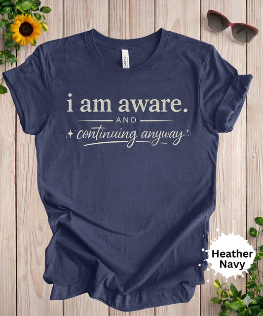 women’s graphic T-shirt featuring the phrase “I am aware and continuing anyway” in a bold and script typography