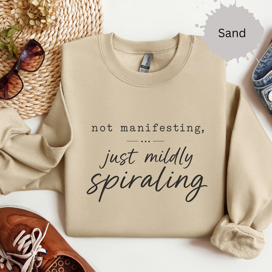 Sweatshirt with light typography reading “not manifesting, just mildly spiraling”