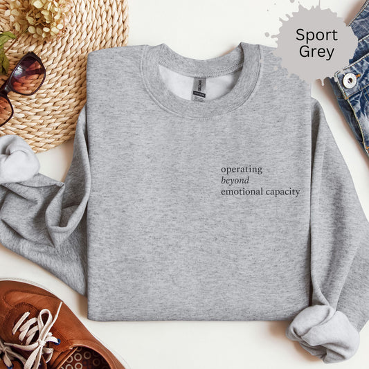 Crewneck sweatshirt with small text reading “Operating beyond emotional capacity.”